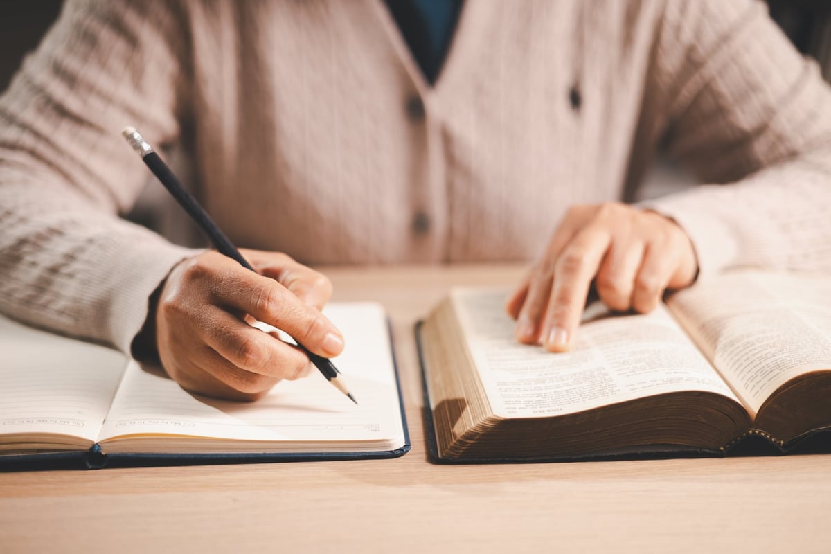 Hands taking notes in a notebook while studying, finger tracking the text in warm light