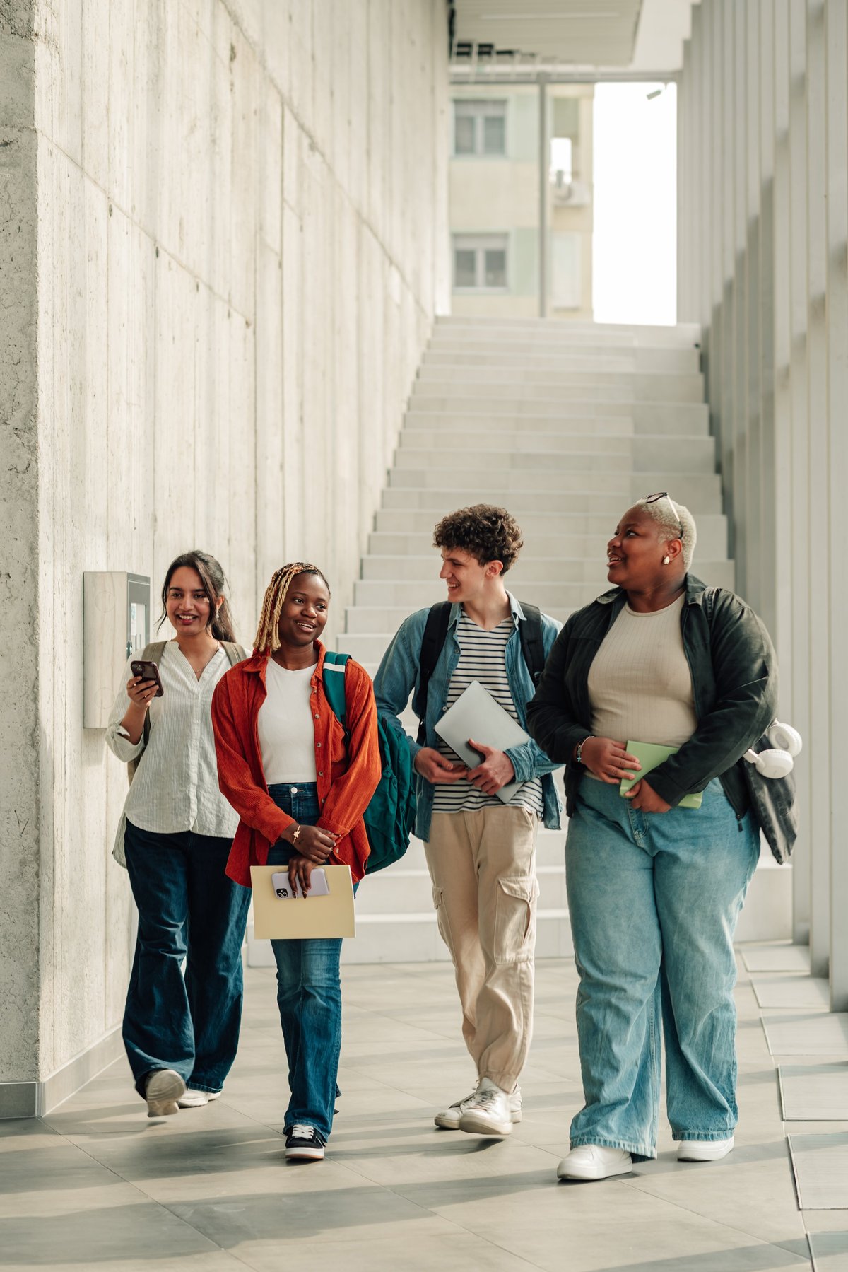 Four young college students walking through a university hall discussing their plans
